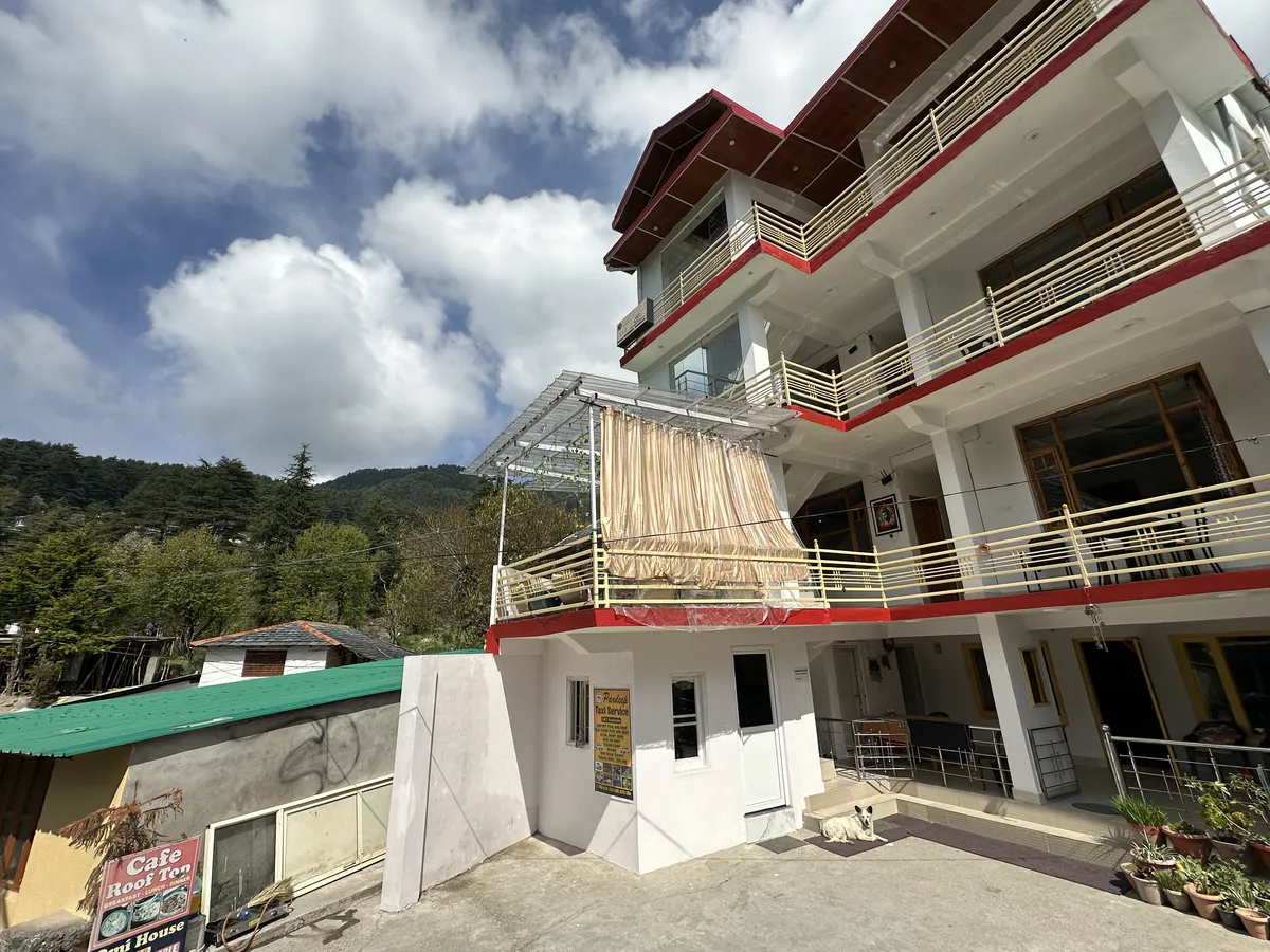 The white OmiHomeStay building with balconies under a cloudy Himalayan sky